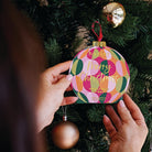 A hand hanging the Circles bauble lip balm box on a Christmas tree.
