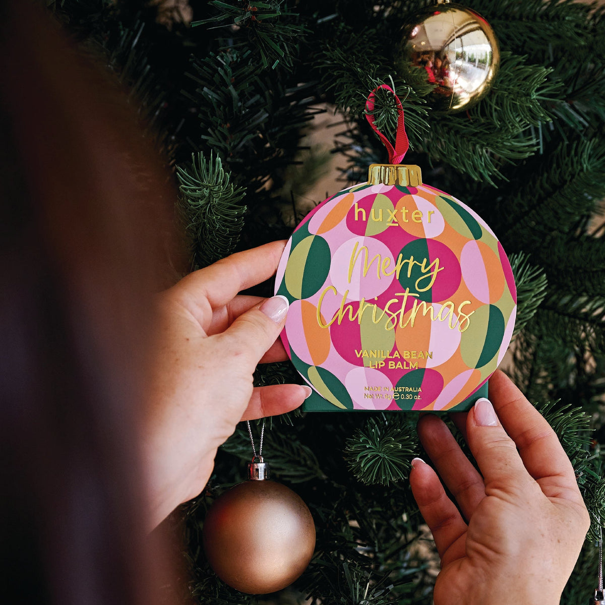 A hand hanging the Circles bauble lip balm box on a Christmas tree.