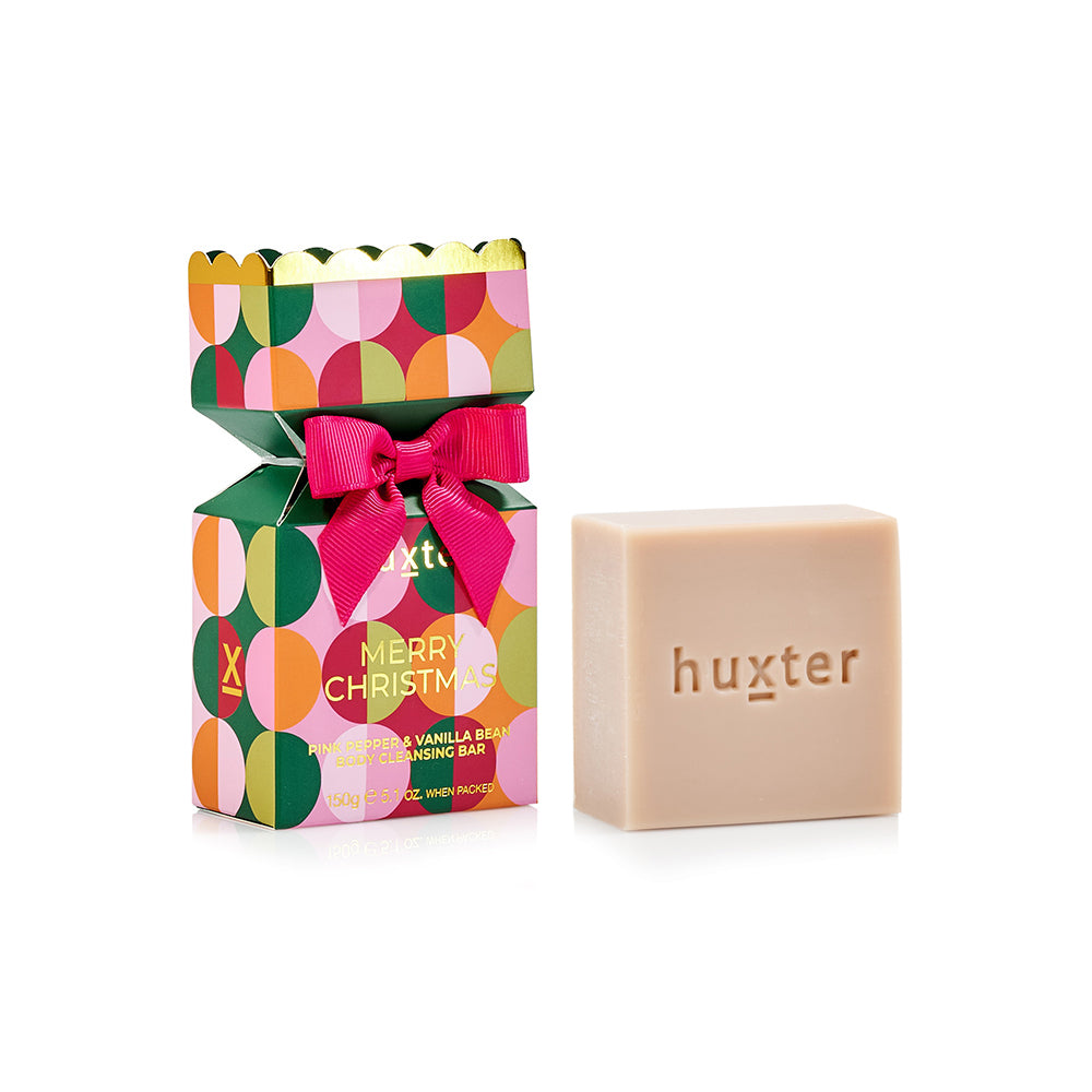 Huxter bon bon box patterned with green, pink and orange circles, pink bow and gold scalloped top, beside the pale cleansing bar stamped huxter.