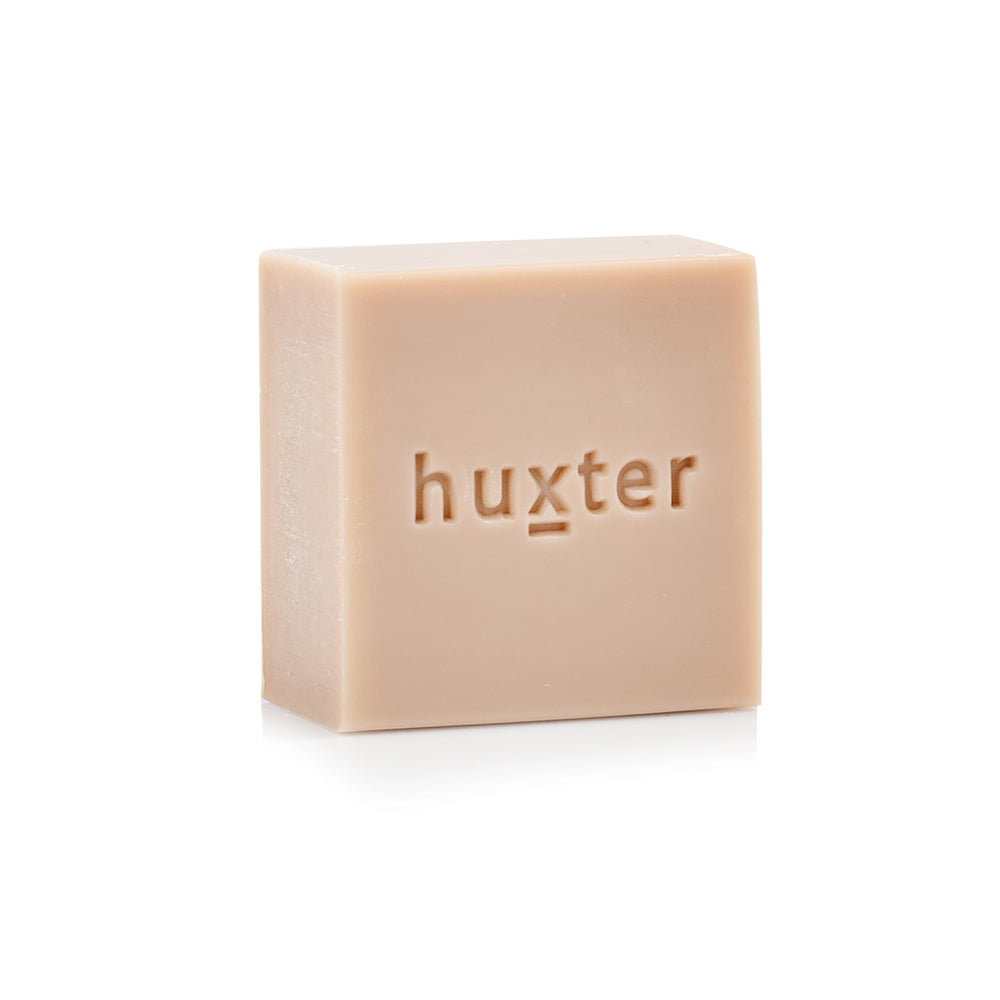 Pale beige 150 g Huxter body cleansing bar with huxter pressed into the face.