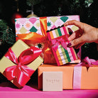 A hand placing the Stripes bon bon cleansing bar box among wrapped presents.