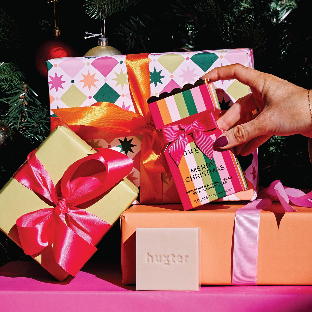 A hand placing the Stripes bon bon cleansing bar box among wrapped presents.
