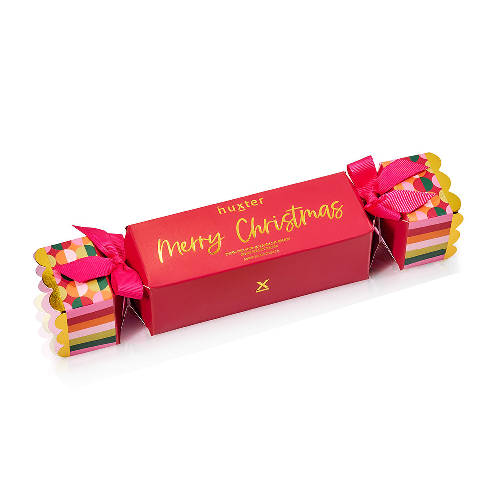 Red Huxter cracker-shaped box with Merry Christmas in gold script and patterned ends tied with pink ribbon.