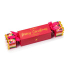 Red Huxter cracker-shaped box with Merry Christmas in gold script and patterned ends tied with pink ribbon.