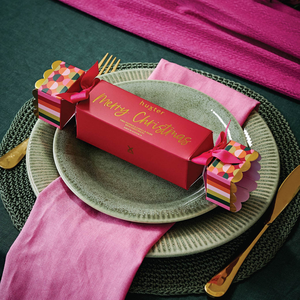The Huxter hand balm cracker laid on a dinner plate with a pink napkin and gold cutlery.