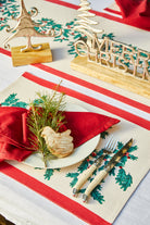 Christmas Foliage placemat under a white plate with a red napkin and cutlery on a Christmas table