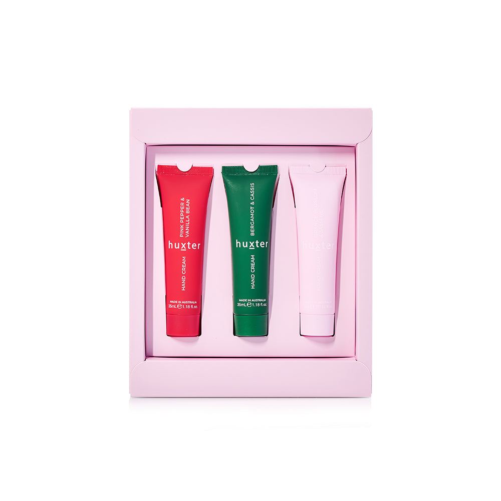 Three 35 mL Huxter hand creams in a pink tray: red Pink Pepper & Vanilla Bean, green Bergamot & Cassis, pale pink Orange Blossom & Jasmine.