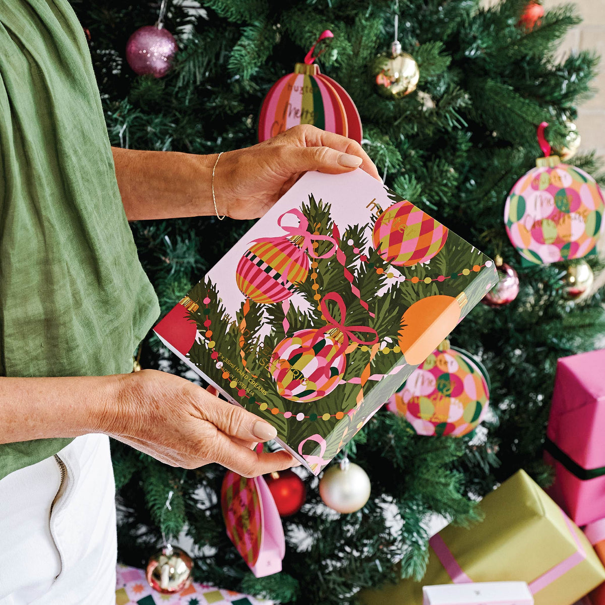 Hands holding the Huxter hand cream trio box in front of a decorated Christmas tree.