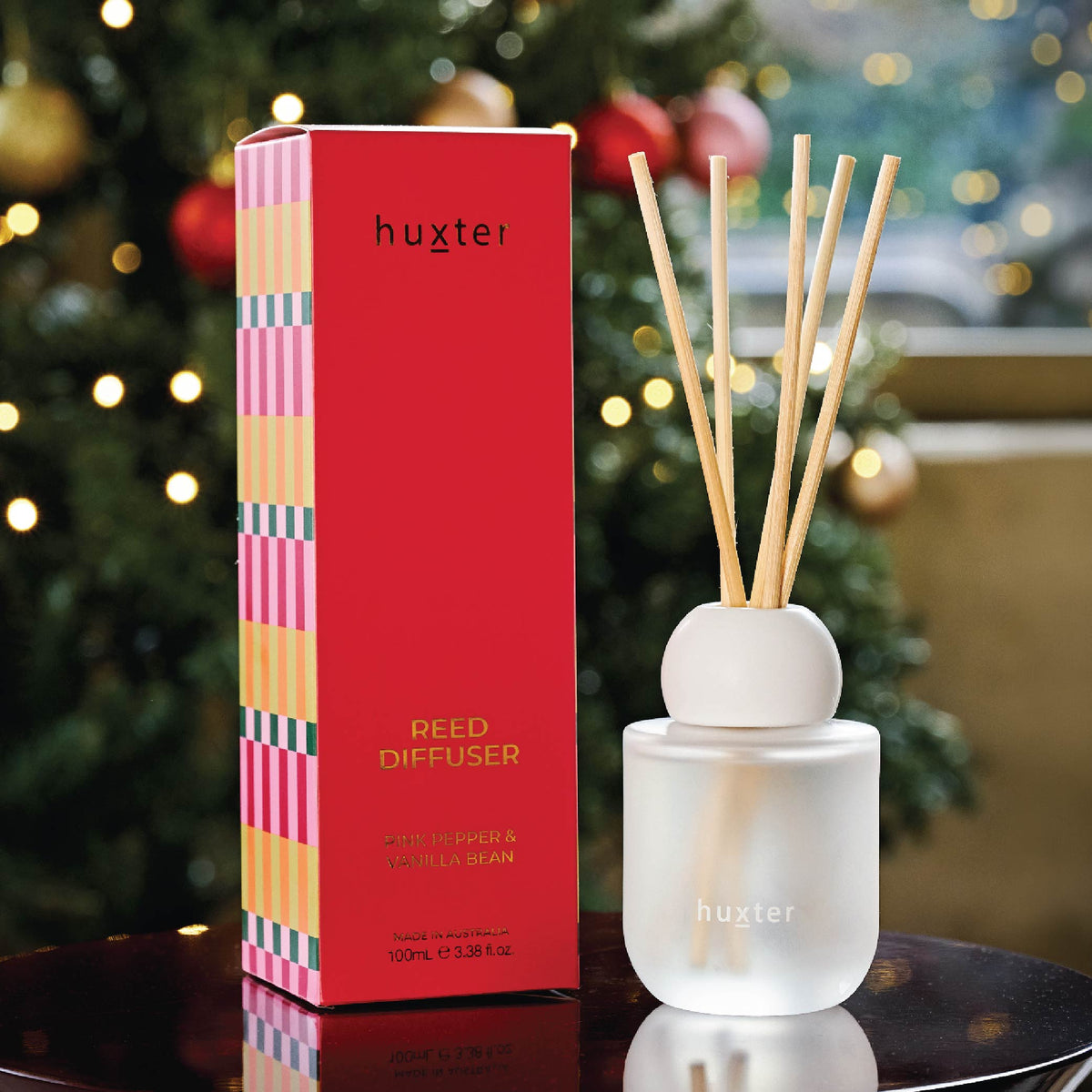The Huxter reed diffuser and its red box on a table in front of a lit Christmas tree.