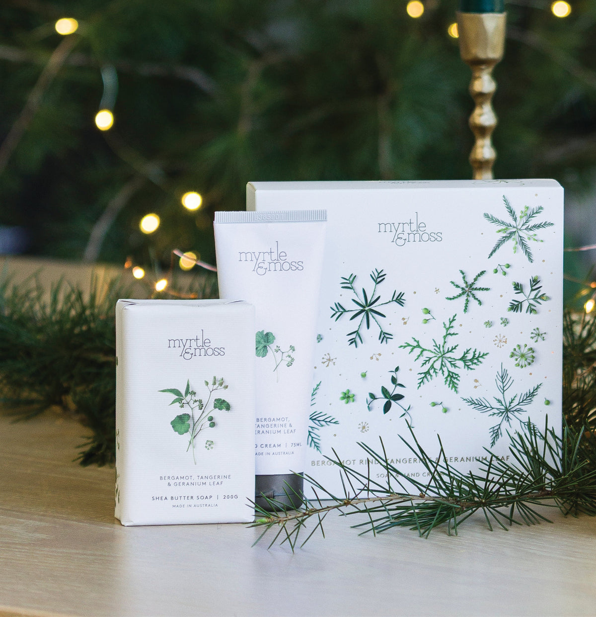 Myrtle & Moss Bergamot Christmas gift box printed with green snowflakes and leaves, with its wrapped shea butter soap and 75 mL hand cream in front.
