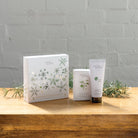The Bergamot soap and hand cream gift box beside the soap bar and hand cream tube on a wooden table.