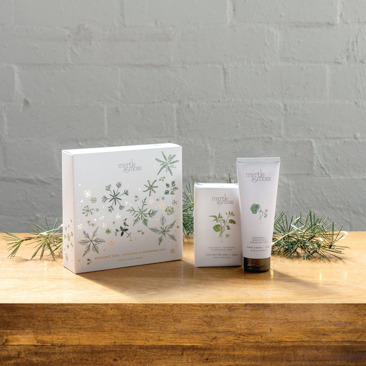 The Bergamot soap and hand cream gift box beside the soap bar and hand cream tube on a wooden table.