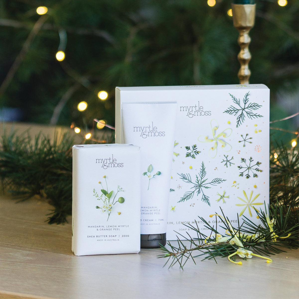 Myrtle & Moss Citrus Christmas gift box printed with green snowflakes and yellow native flowers, with its wrapped shea butter soap and 75 mL hand cream in front.