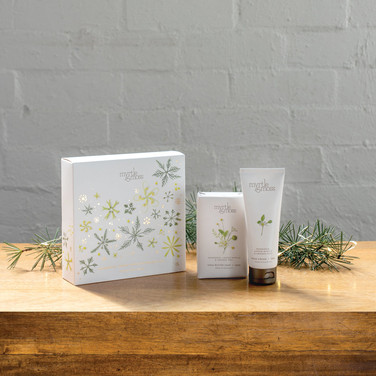 The Citrus soap and hand cream gift box beside the soap bar and hand cream tube on a wooden table.