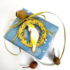 The Cockatoo ornament tied with gold ribbon onto a blue wrapped gift, gum nuts beside it.