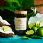 Coconut & Lime candle on teal with whole and halved limes, coconut and crushed ice