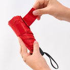 Two hands sliding the red umbrella out of its matching fabric sleeve.
