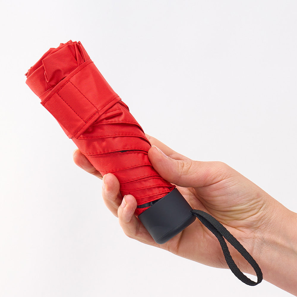 A hand holding the folded red umbrella, showing how small it packs down.
