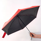 A red umbrella held open from below, showing the black UV-protective underside of the canopy.