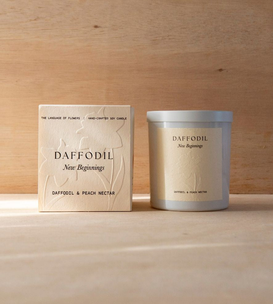 The Daffodil candle in its white vessel beside its cream box.