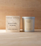 The Daffodil candle in its white vessel beside its cream box.