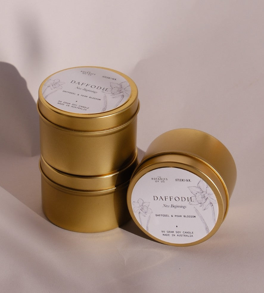 Three gold Daffodil travel tins, one tipped forward to show its lid label with a drawing of the daffodil.