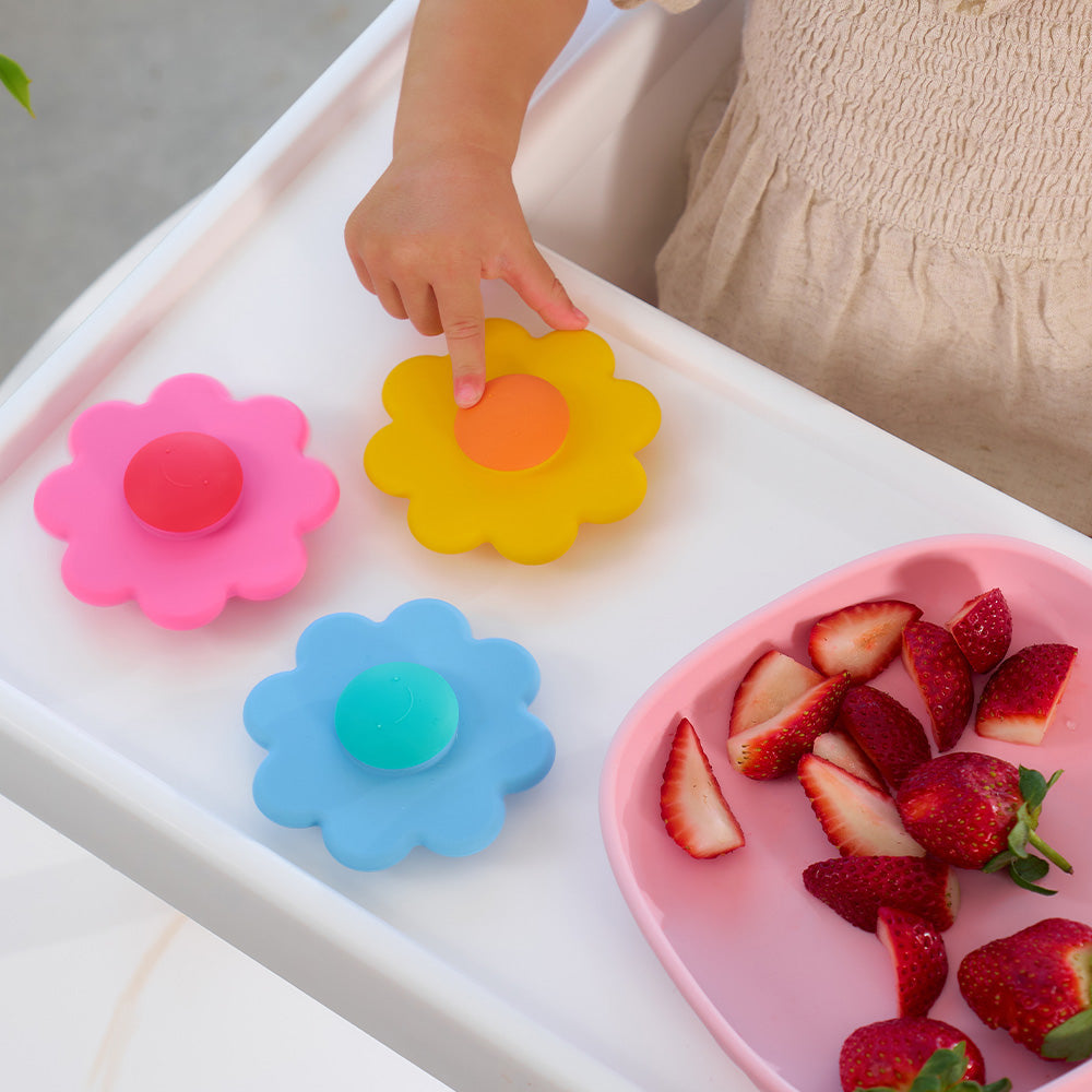 Child's hand spinning a yellow daisy spinner on a white tray beside strawberries