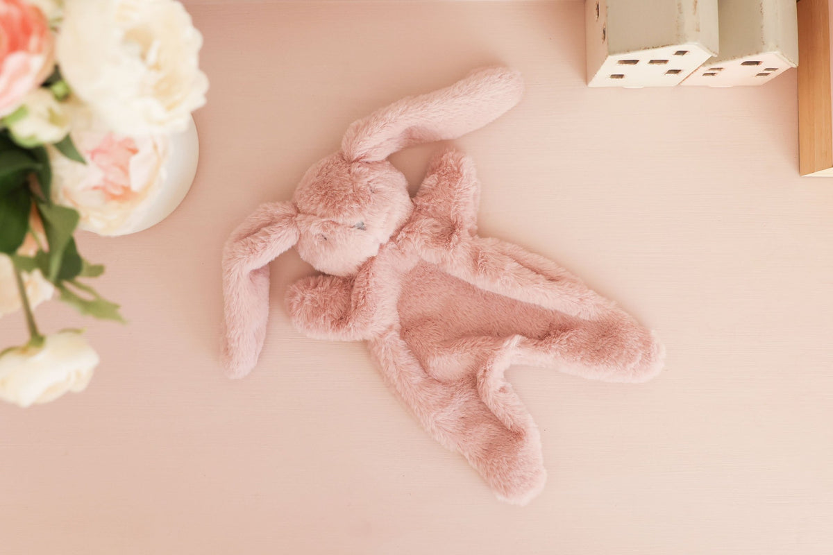 The petal pink bunny comforter lying on a pink surface beside fresh flowers.