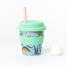 Dino babychino cup: dinosaur print on sky blue with a mint lid and wavy sleeve, a beige straw and a marshmallow beside it