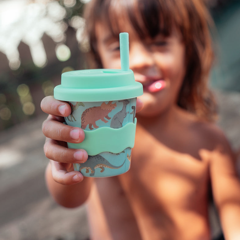 Child holding up the Dino babychino cup with a mint straw