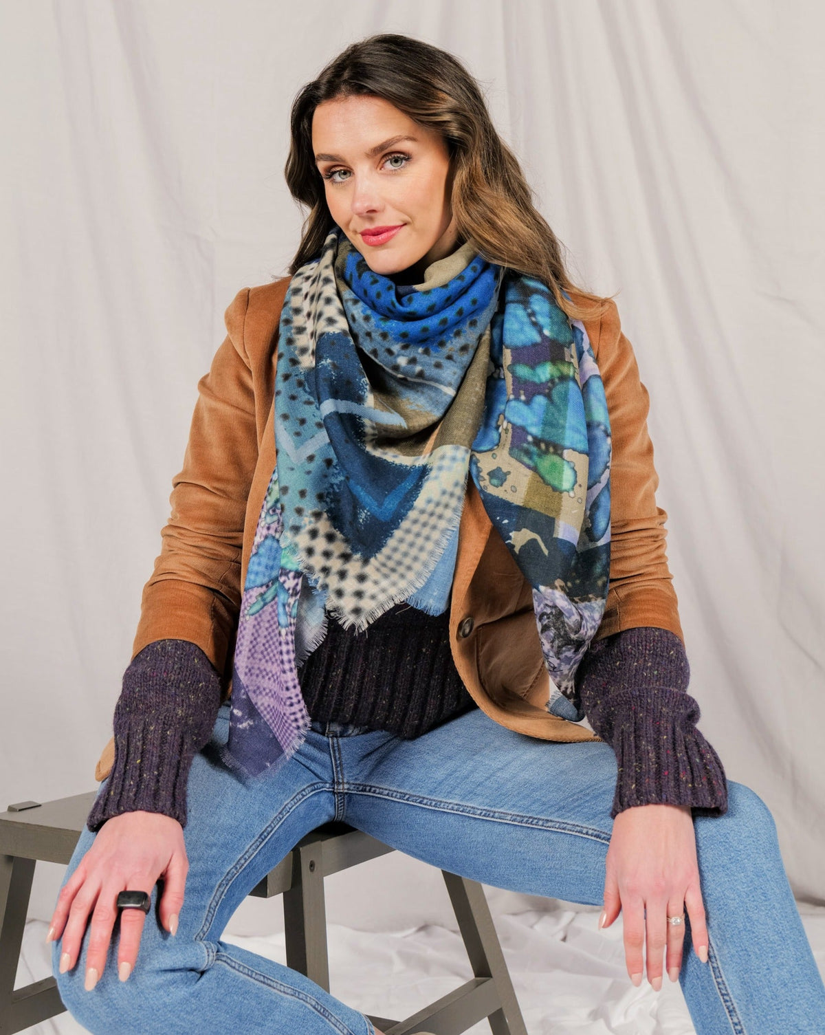 Model in a tan leather jacket wearing the blue patchwork print scarf knotted at the neck