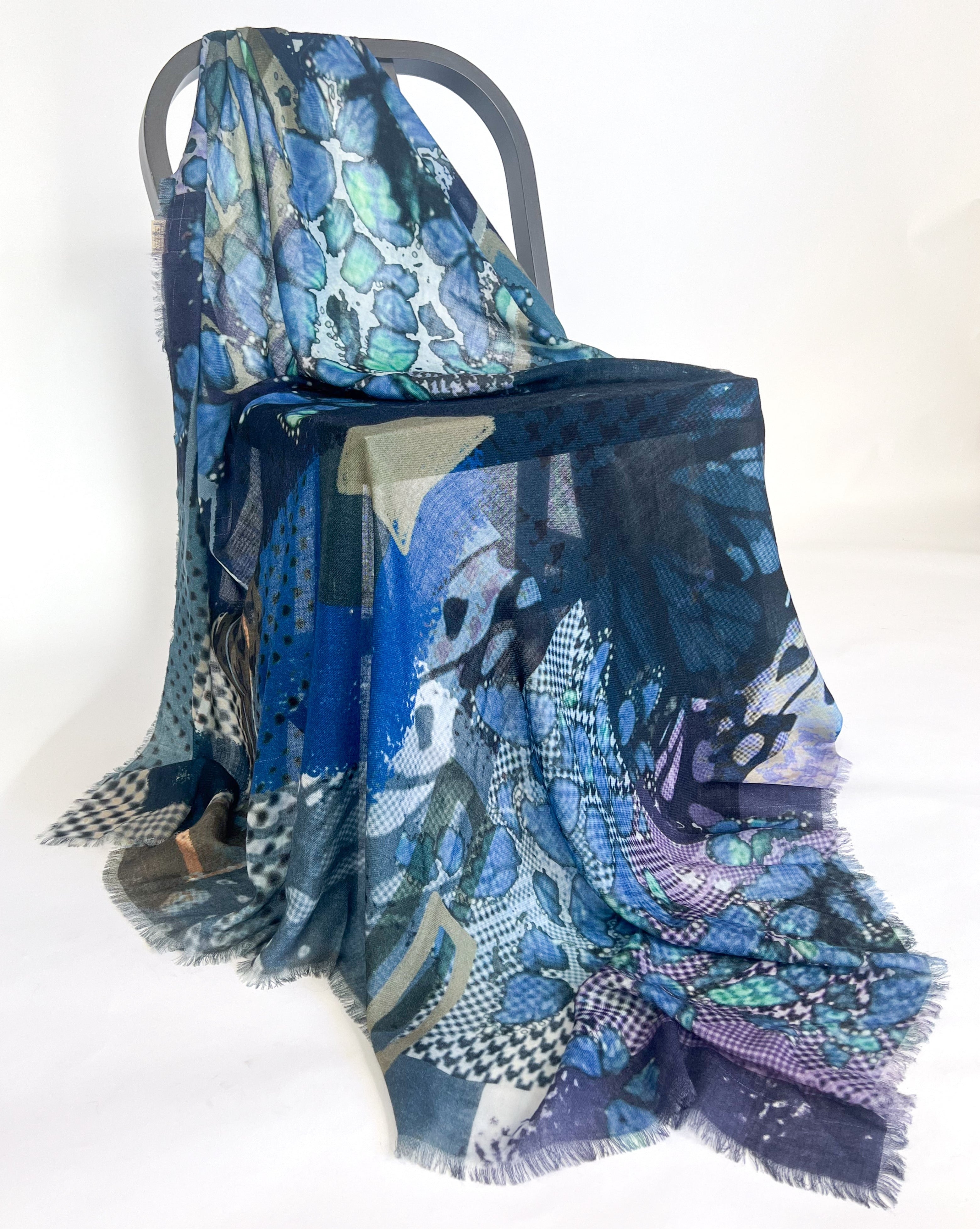 The blue patchwork scarf draped over a grey chair, showing its fine fringed edge