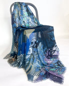 The blue patchwork scarf draped over a grey chair, showing its fine fringed edge