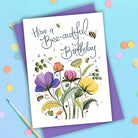 Card lettered Have a Bee-autiful Birthday above purple and yellow flowers and bees, on a purple envelope