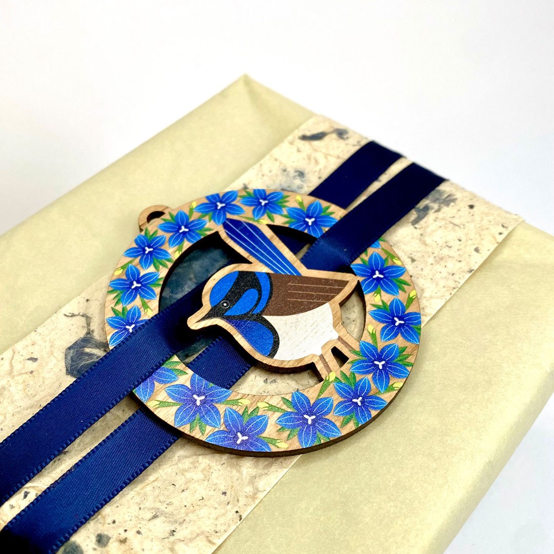 The fairy wren ornament tied with navy ribbon onto a wrapped gift.