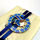 The fairy wren ornament tied with navy ribbon onto a wrapped gift.