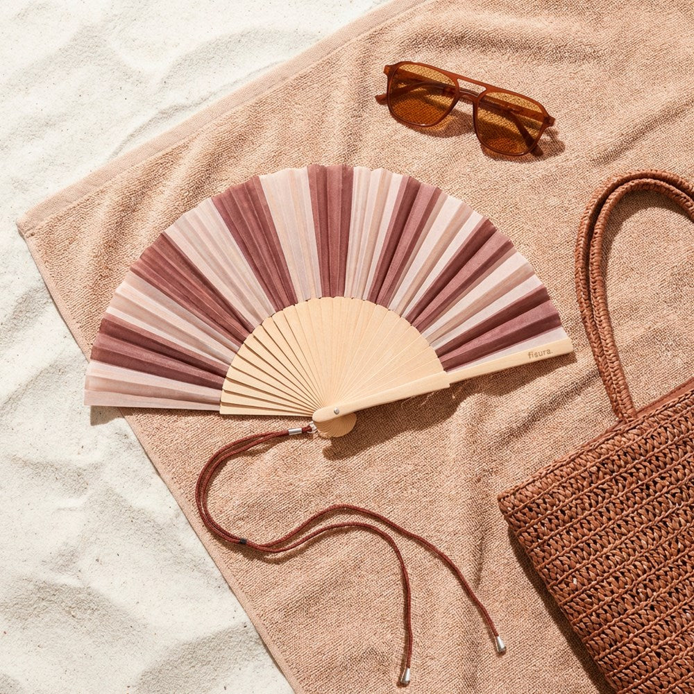 Striped fan lying open on a beach towel beside sunglasses and a woven bag