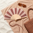 Striped fan lying open on a beach towel beside sunglasses and a woven bag
