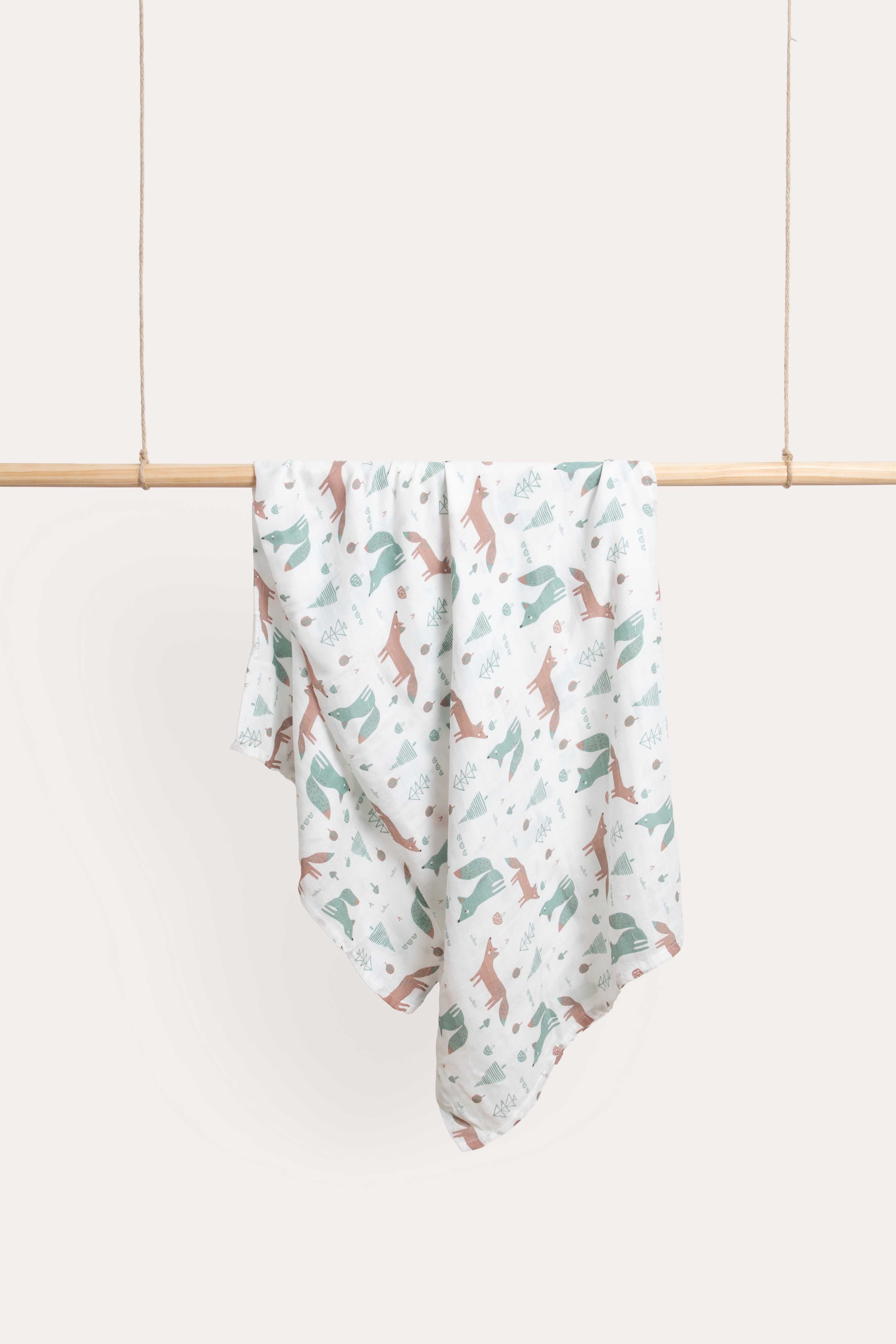 Foxie muslin wrap hanging over a timber rail, printed with sage and terracotta foxes on white.