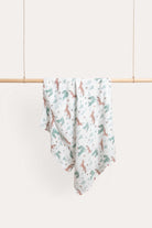 Foxie muslin wrap hanging over a timber rail, printed with sage and terracotta foxes on white.