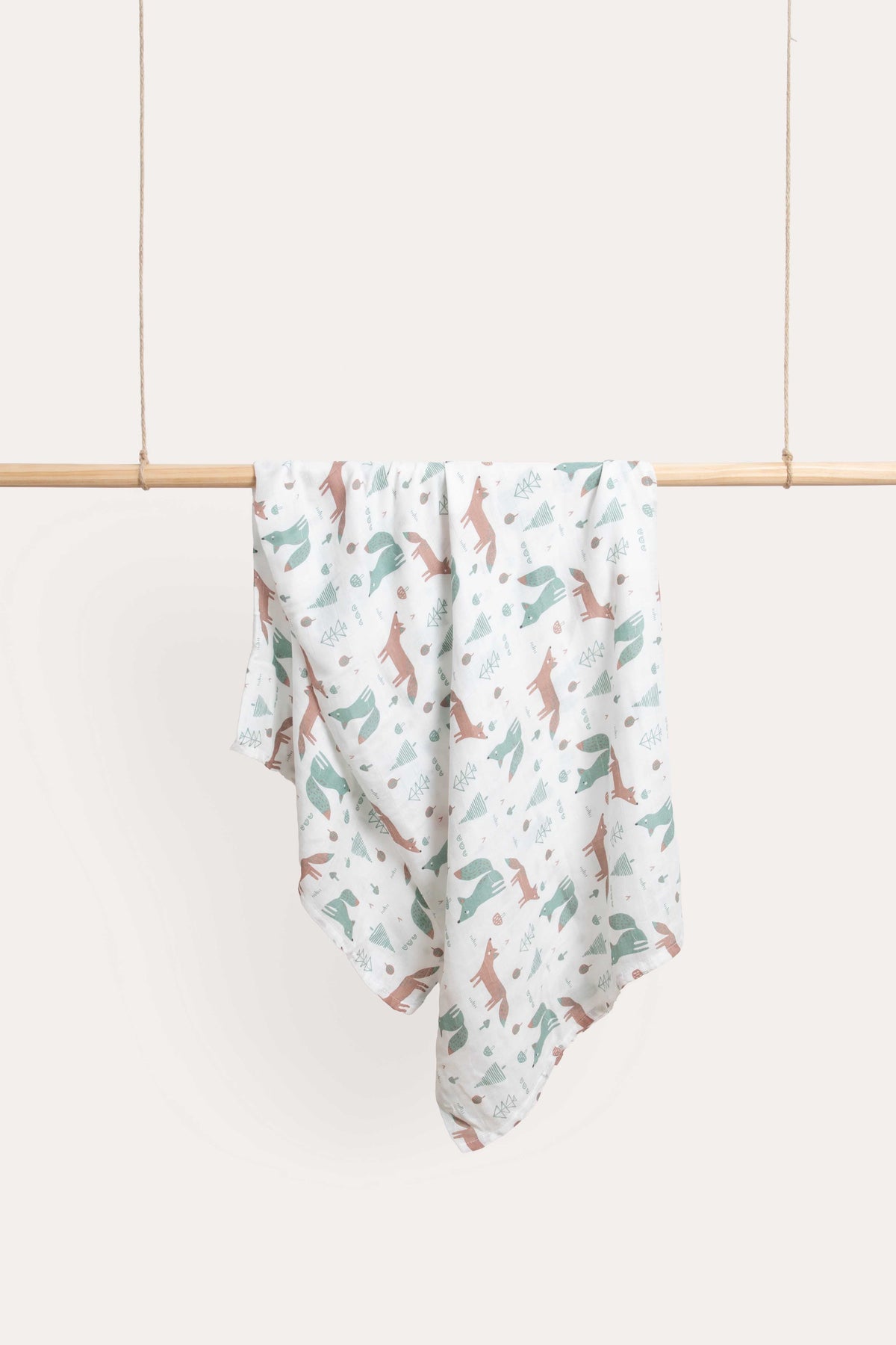 Foxie muslin wrap hanging over a timber rail, printed with sage and terracotta foxes on white.