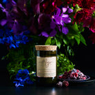 Violet & Frosted Berries candle in a reclaimed wine bottle beside purple blooms and a dish of frozen berries