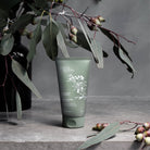 The green hand scrub tube among eucalyptus leaves and gum nuts on a concrete shelf.