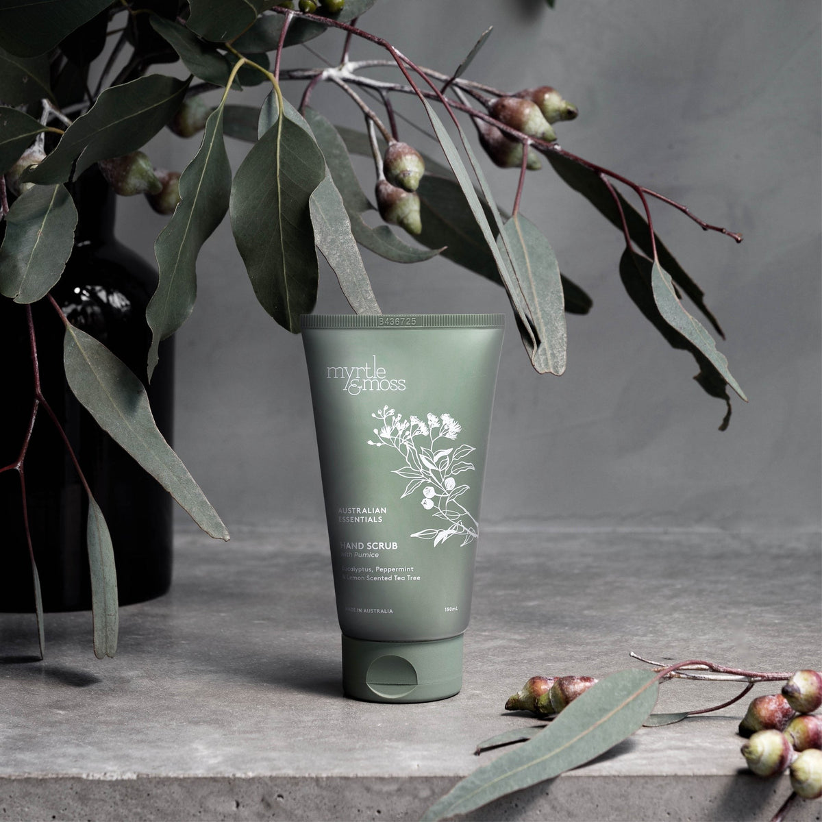 The green hand scrub tube among eucalyptus leaves and gum nuts on a concrete shelf.