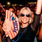 Woman in sunglasses at an evening concert holding up the I love Siesta fan
