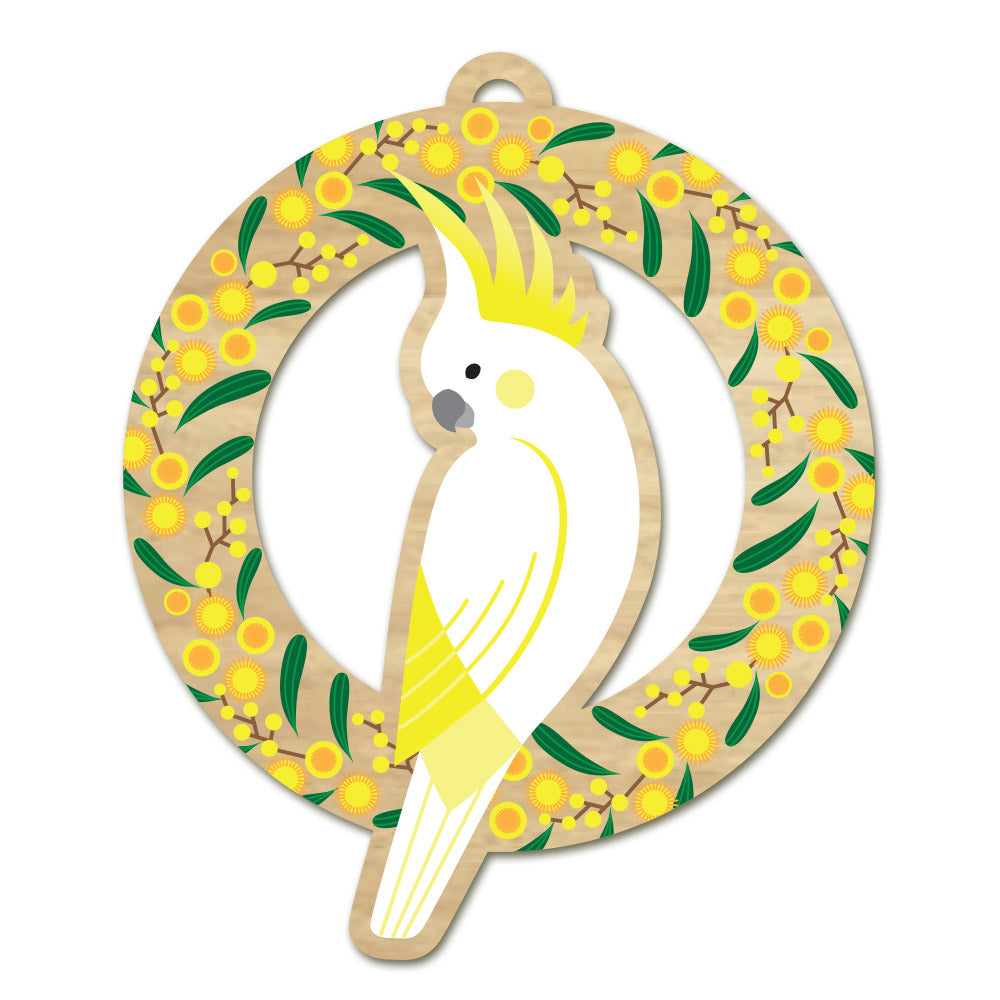 Round wooden Christmas ornament: a white sulphur-crested cockatoo inside a wreath of yellow golden wattle blossom