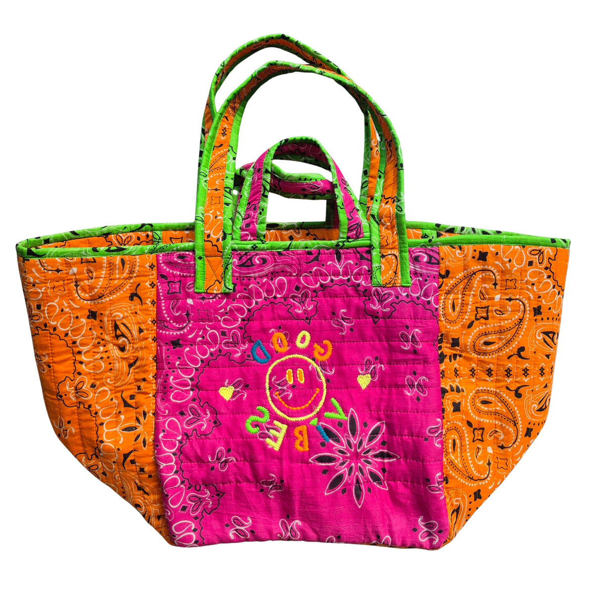 One quilted cotton tote with orange paisley bandana sides and a hot pink front embroidered with a smiley face and GOOD VIBES, with long lime-trimmed shoulder handles and short pink handles on the front.