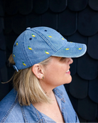 Woman in a denim shirt wearing the yellow-lemon denim cap in profile against a dark shingled wall.
