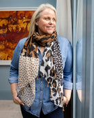 Woman in a denim shirt wearing the leopard and spot scarf hanging long over a dark top.