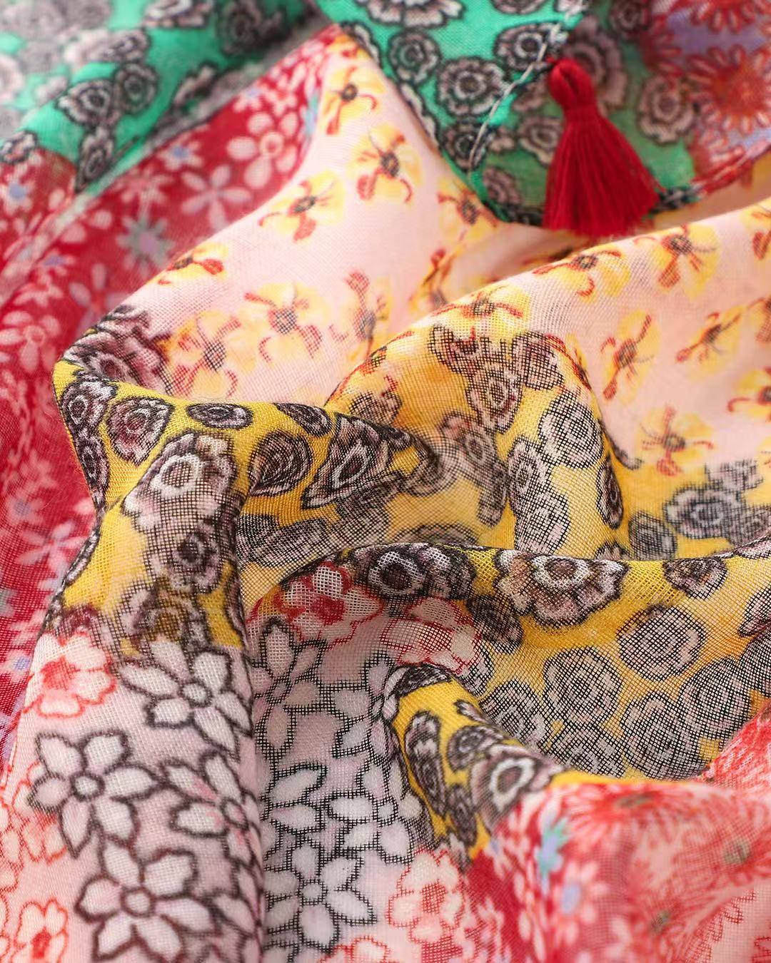 Close-up of the red patchwork scarf showing the pink, yellow and cream ditsy floral panels and a red tassel.